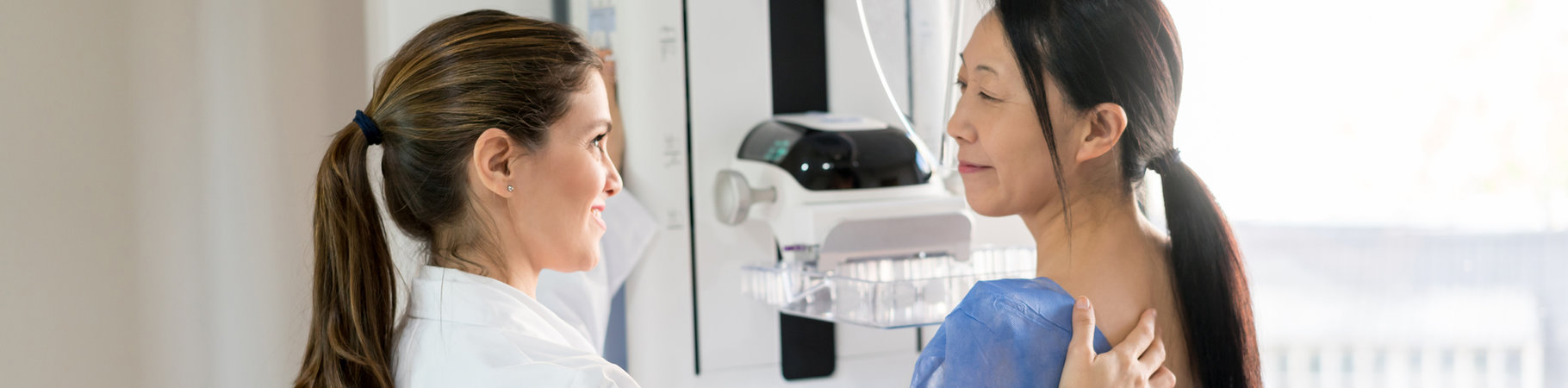 Friendly female doctor talking to her patient and adjusting her to do a mammogram at the clinic