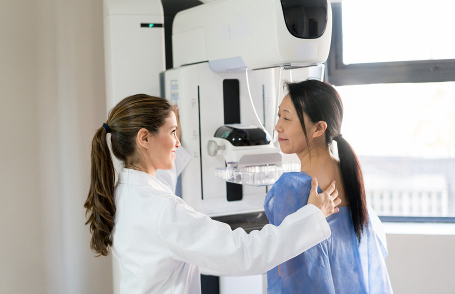 Friendly female doctor talking to her patient and adjusting her to do a mammogram at the clinic